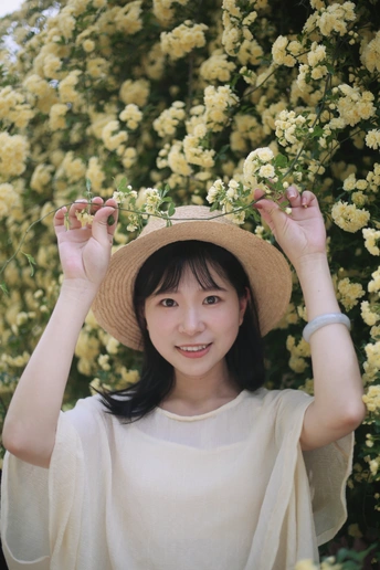 一位穿着白帽子站在黄色玫瑰丛前的年轻女子