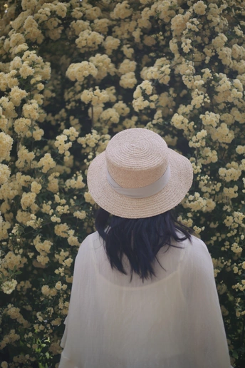 一位戴白帽子的女士站在一片黄花的田野前