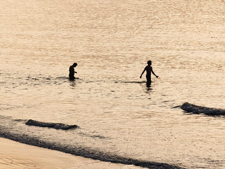 一个男子和一个孩子站在海洋中 一个男子和一个男孩沿着海滩走 带着冲浪板在一个水域中。