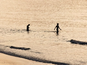 一个男子和一个孩子站在海洋中 一个男子和一个男孩沿着海滩走 带着冲浪板在一个水域中。