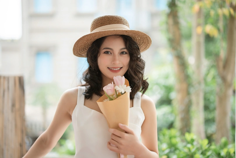 一位身穿白色连衣裙、戴着帽子、手里拿着一束粉色花朵的年轻女子的肖像