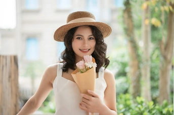 一位身穿白色连衣裙、戴着帽子、手里拿着一束粉色花朵的年轻女子的肖像