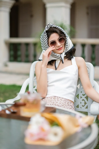 一个戴着帽子和太阳镜的女人坐在外面的一张桌子旁 桌子上摆着食物