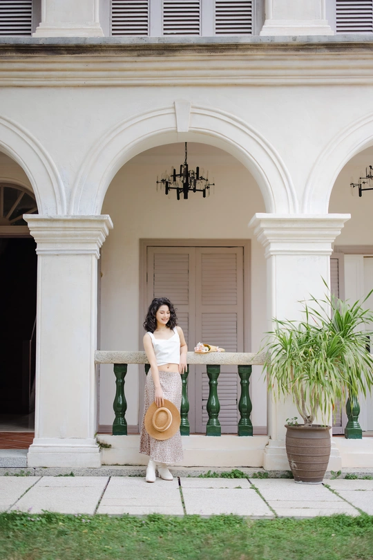 一个穿着白色连衣裙、戴着帽子的年轻女子站在一所房子的院子里