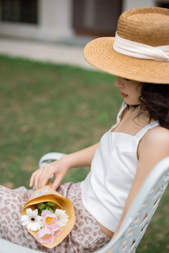 一位身穿白色连衣裙、头戴草帽的年轻女子坐在白色椅子上 手里拿着一朵花