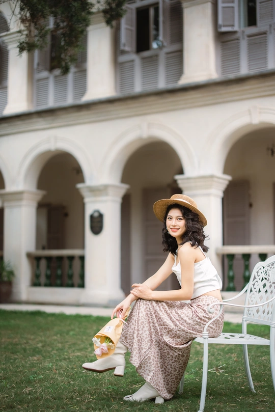 一个穿着连衣裙、戴着帽子的年轻女子坐在院子里的白色长椅上 手里拿着一个包坐在草地上