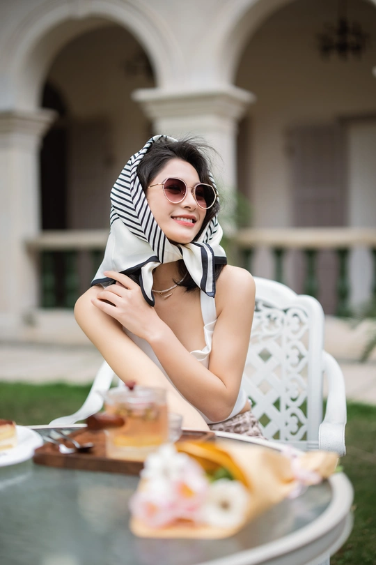 一个戴着墨镜和围巾的年轻女子拿着一盘食物坐在外面的桌子旁