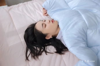 一个年轻女子躺在带有白色枕头和毛毯的床上