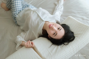 一位穿着睡衣的年轻女子躺在白色的床垫上 正在看相机。