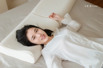 一个年轻女子躺在白色床垫上 床单和枕头都是白色的 正在看相机。