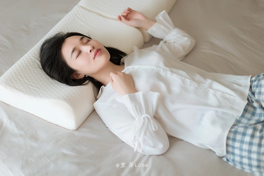 一个穿着白衬衫的年轻女子躺在床上 床上有白色的毛毯和枕头。