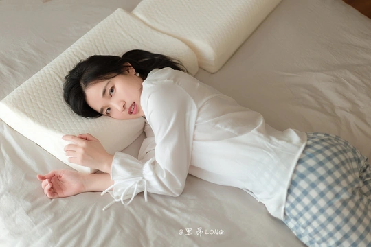 一个穿着睡衣的年轻女子躺在白色的床垫上 床垫上铺着白色的床单和枕头。