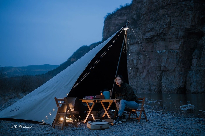 一位妇女在帐篷前夜间的桌子旁坐着