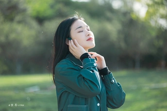 美丽的年轻女子穿着一件绿色夹克在公园里用手机聊天