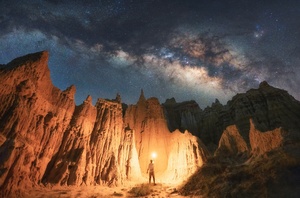 一个人站在山顶上 夜晚拿着灯笼 天空中星星闪烁。