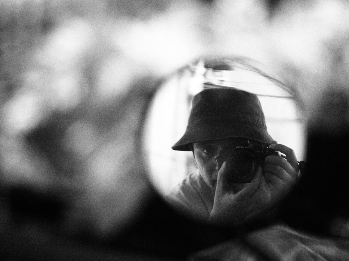 一张黑白照片 照片中一名戴帽子的男子拿着相机对着汽车后视镜
