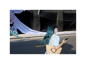 一位戴蓝发饰、戴口罩的女子走在街上 低头看手机。