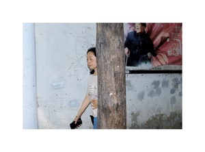 一位年轻女子靠在一根柱子旁边 墙上有一张照片。
