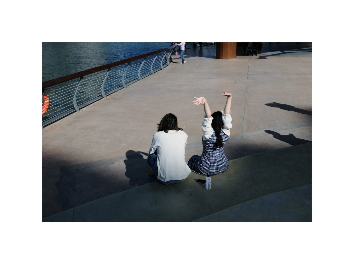 一些年轻女子坐在地上 双手举高 水边的阴影投射在地上。