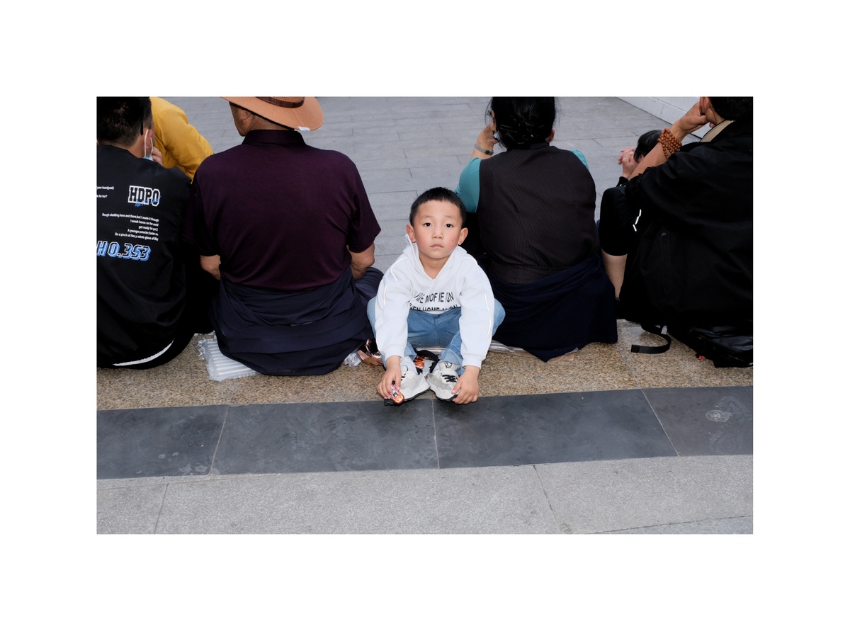 一个年轻的男孩坐在水泥人行道地板上 一个男子坐在他身后 坐在台阶上 把他的鞋子放在地板上。