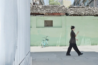 一位女士走在城市的一条街道上 旁边有一面绿色的墙。