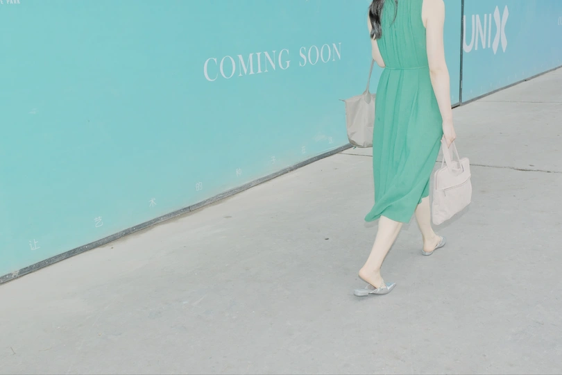 一位穿着绿色连衣裙的女人站在蓝色墙壁前行走