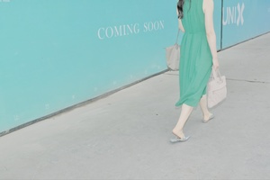 一位穿着绿色连衣裙的女人站在蓝色墙壁前行走
