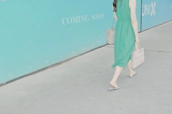 一位穿着绿色连衣裙的女人站在蓝色墙壁前行走