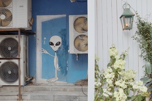 一座蓝色的房子 墙上有一幅骷髅的壁画 门旁边有一台风扇。