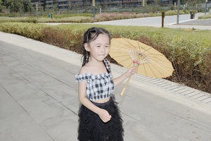 一个穿着黑色连衣裙的小女孩站在人行道上 手里拿着一把雨伞。