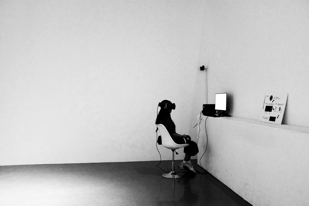 一个房间的角落 一个人坐在椅子上 前面有一台电脑 墙上有一部电话。