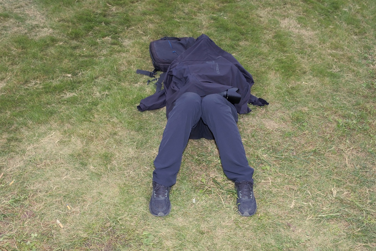 一个穿着西装的男人躺在草地上 带着一把伞和背包。