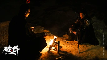 一个男子和一名女子坐在夜晚的山洞里的篝火旁边。