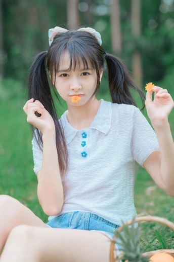 一个年轻女孩坐在公园里的草地上吃橘子 旁边是一篮水果