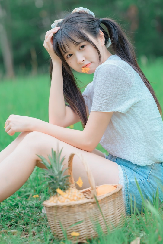 年轻漂亮的女人坐在森林里一篮菠萝旁的草地上