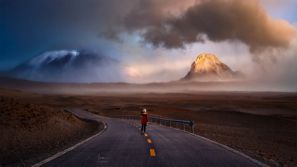 一个人在有山和云朵的背景下的路上行走