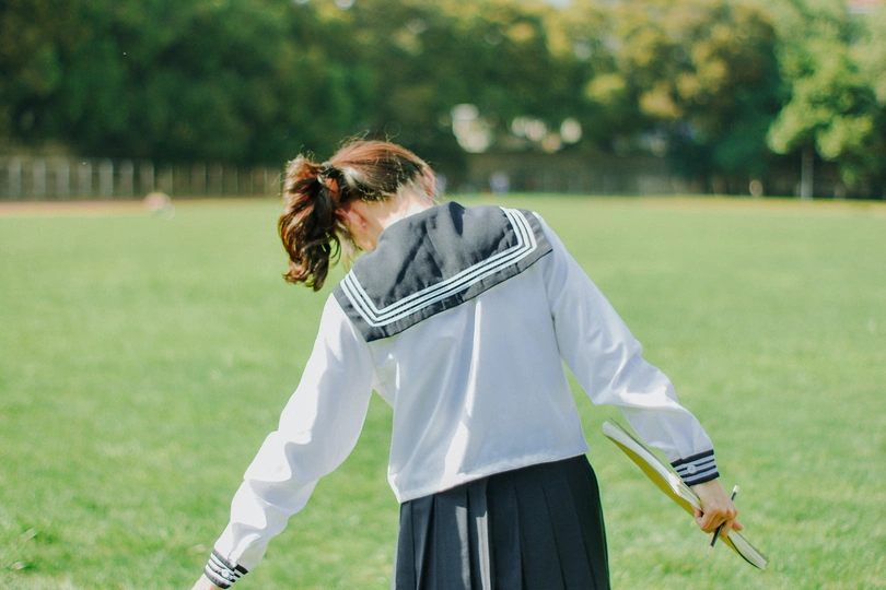 一个穿着校服的年轻女孩手持宝剑站在绿草地上