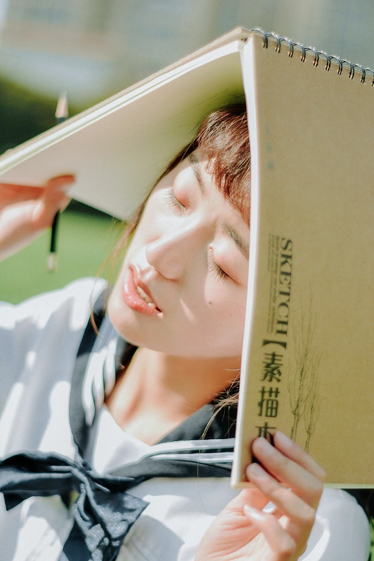 一个戴帽子正在草地上阅读一本书的年轻女子