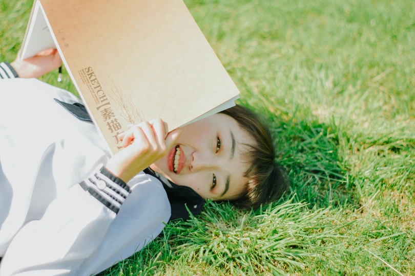 一个年轻女子躺在草地上 一本书放在她的头上和脸上阅读。