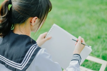 一个年轻女孩坐在草地上 在一张纸片上写在一本笔记本上。
