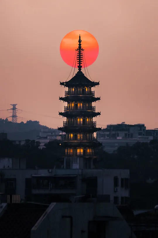 夕阳西下时 太阳升起在城市上 前景是一座寺庙的塔。