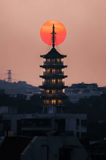 夕阳西下时 太阳升起在城市上 前景是一座寺庙的塔。
