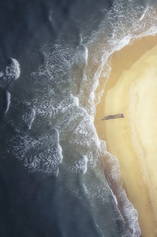 一片沙滩上有一艘船在岸边 水中有波浪的空中视角