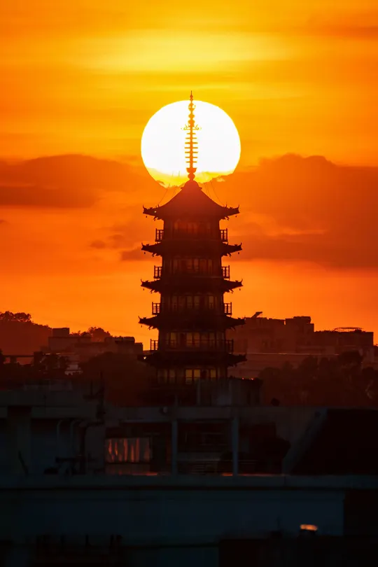 夕阳下 太阳升起在城市的上空 前景中有塔或结构。