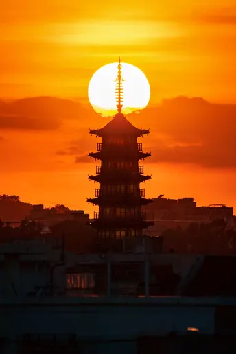 夕阳下 太阳升起在城市的上空 前景中有塔或结构。