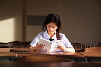 一个年轻女孩坐在教室的桌子旁读书