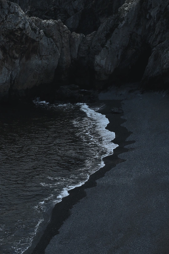 一个黑暗的海滩 夜晚有黑色的沙子、岩石和水体。