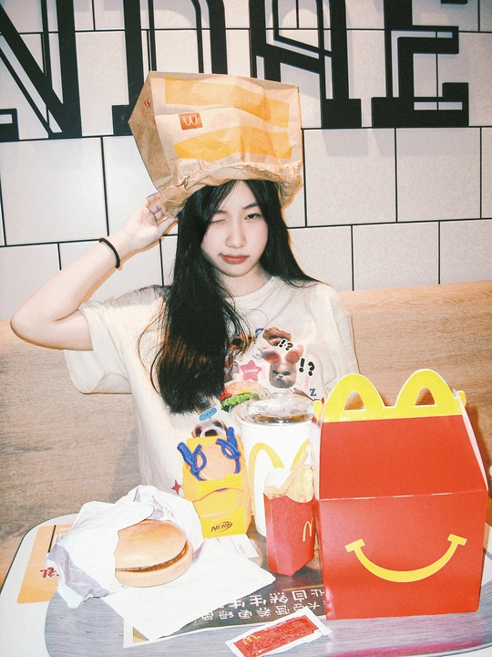 一个年轻女子坐在桌子上 头上放着食物和玩具 脸上盖着纸袋。