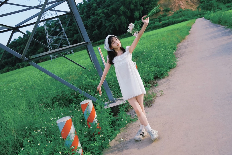 一位穿着白色连衣裙的年轻女子站在一条路上