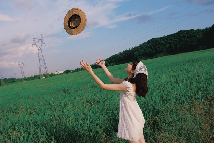 一位穿着白色连衣裙的年轻女子 戴着帽子 站在一片绿色草地上。